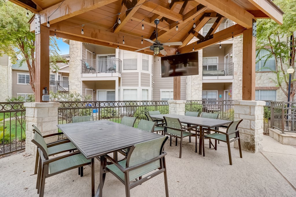 a patio with tables and chairs and a wooden gazebo with a television