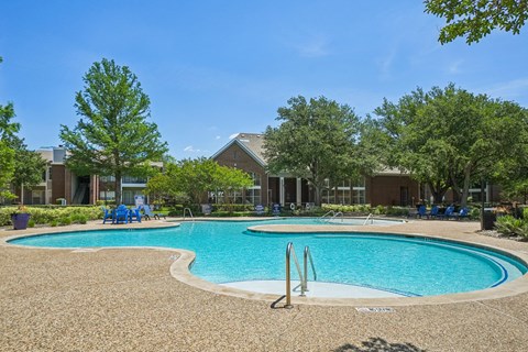 Resort-style pool with curved edges, lounge seating, trees, and clubhouse views.