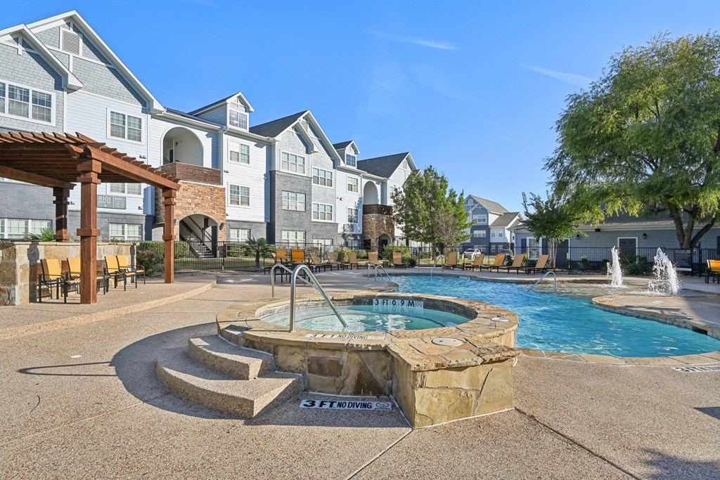 A pool area with a hot tub and a fountain in front of apartment buildings.