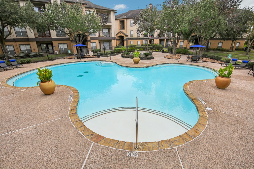 A large outdoor swimming pool surrounded by a concrete patio and a grassy area with trees.