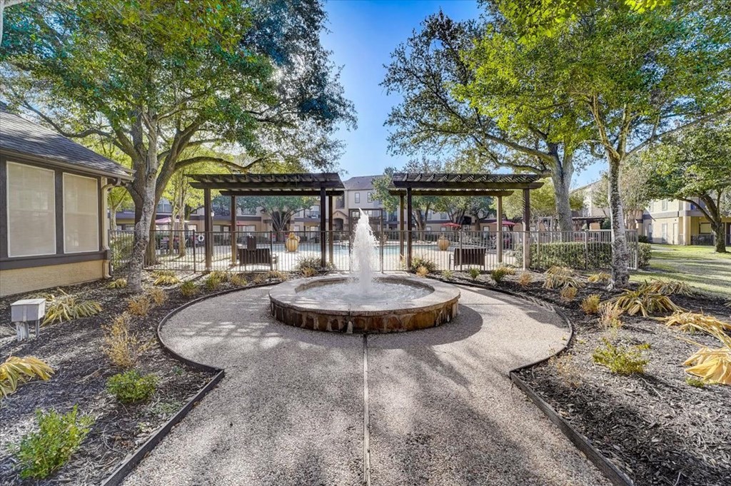 a fountain in the middle of a park with benches and trees