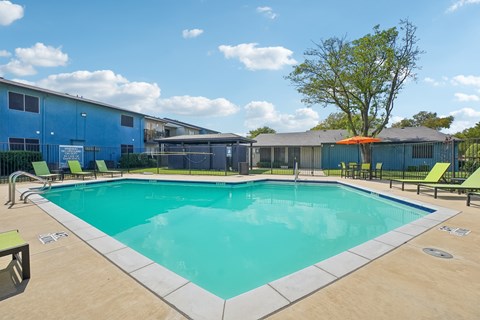 A large outdoor swimming pool surrounded by a fence and lounge chairs.