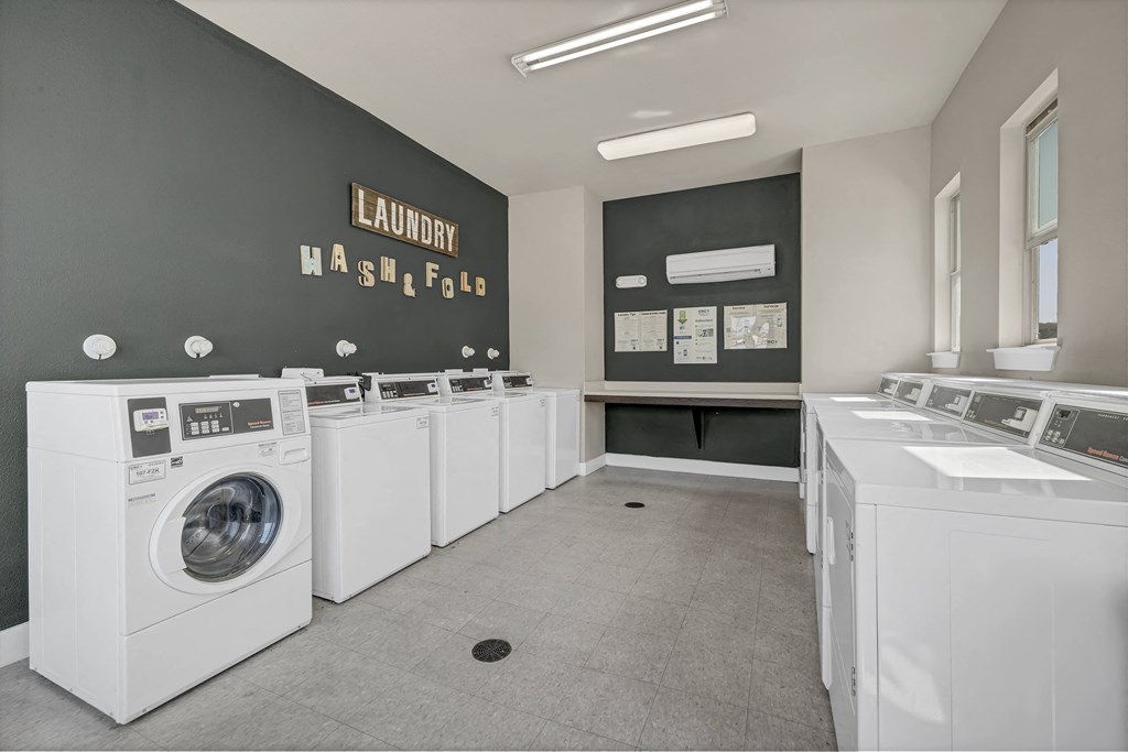 a washer and dryer room with a row of white washing machines and sinks