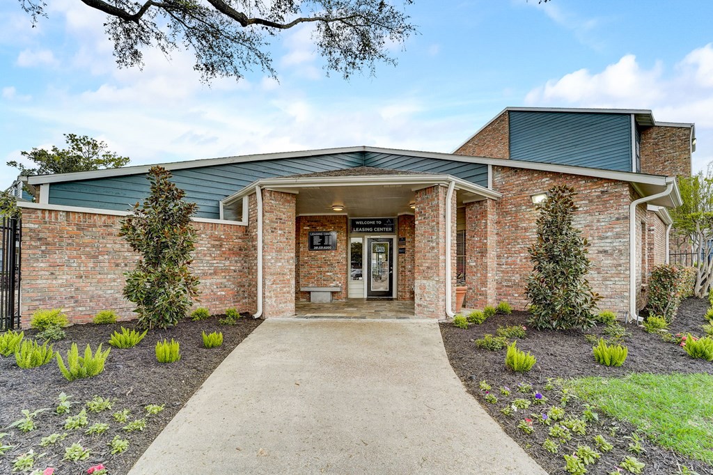 the front of a brick building with a walkway and plants