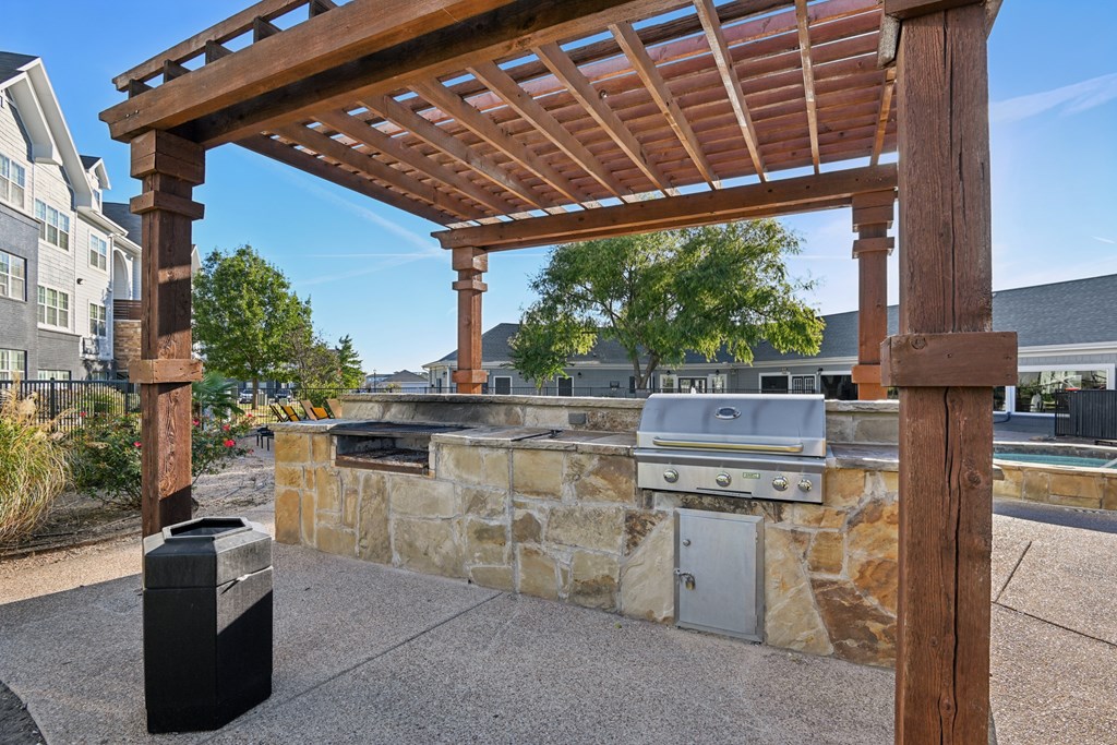 A wooden pergola is over a stone wall with a grill underneath it.