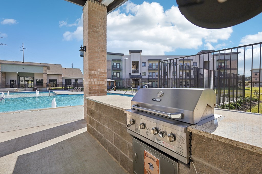 a grill on a patio next to a pool with a building in the background