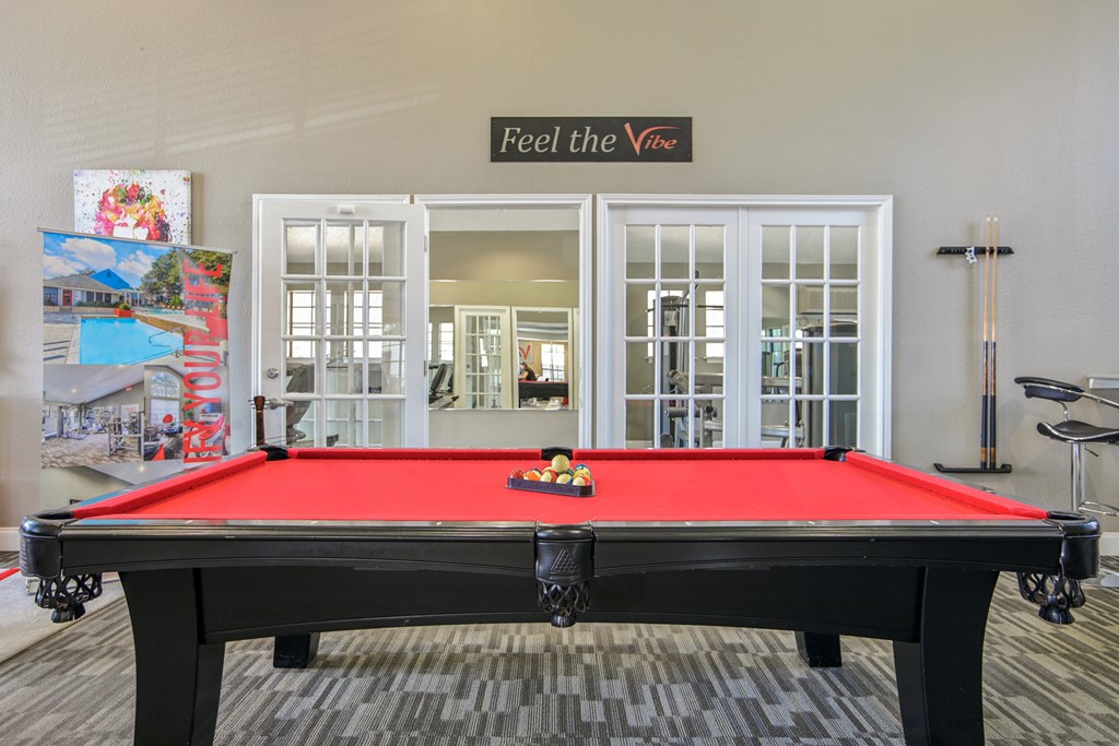 A pool table with a red cloth and a sign that says "Feel the Vibe" above it.
