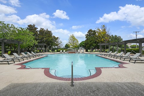 A large pool surrounded by lounge chairs and trees.