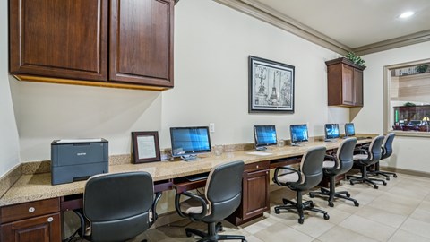 A row of computers are on a desk in a room with wood paneling.