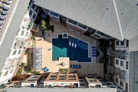 A swimming pool is surrounded by a small building and a parking lot.