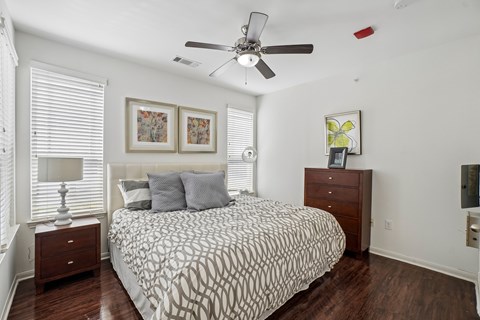 A bedroom with a patterned bedspread, a ceiling fan, and a nightstand with a lamp.