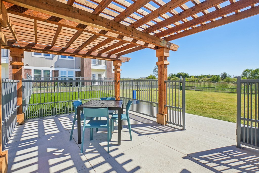 A wooden pergola with a table and chairs is set up on a patio.