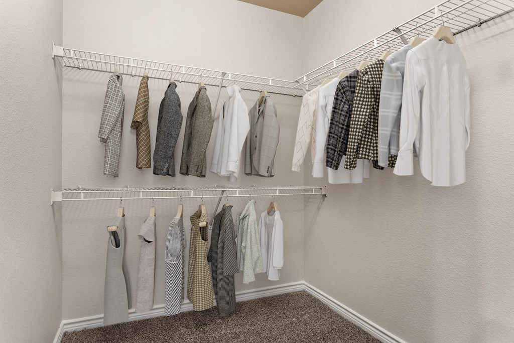 a walk in closet with white walls and a white rod with clothes hanging on it