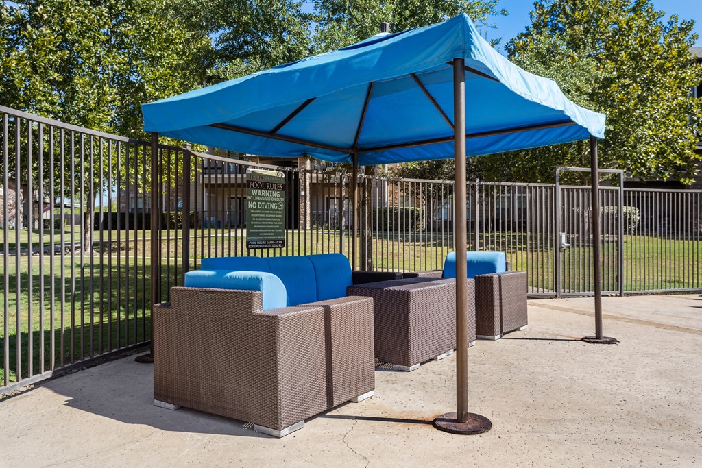 a blue umbrella and three couches in front of a fence