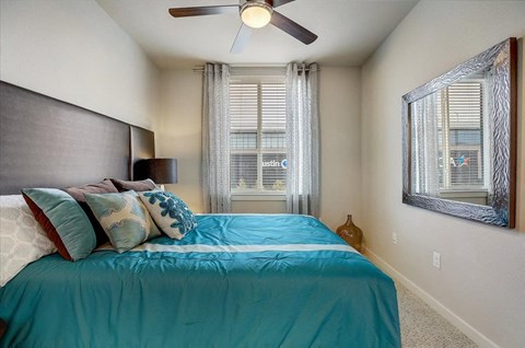 Cozy bedroom with ceiling fan, accent pillows, and large window with curtains.
