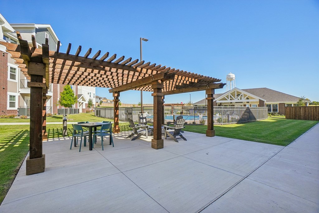 A wooden pergola is over a table and chairs in a courtyard.
