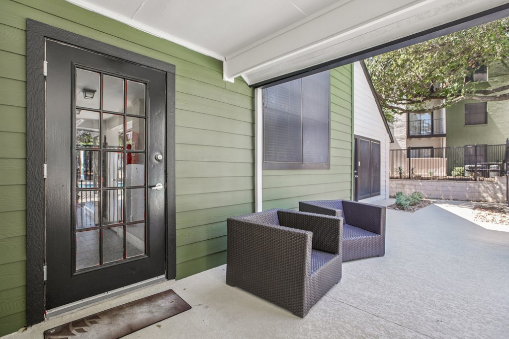 A patio with a black door and two chairs.