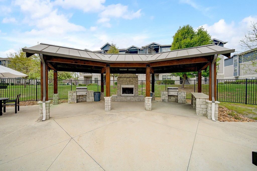 a covered patio with a stone fireplace and a pavilion