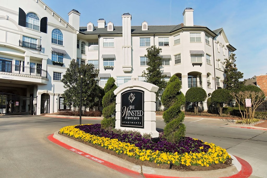 a large white building with a sign in the middle of a roundabout with flowers