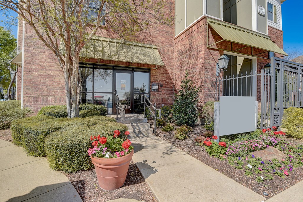a sidewalk in front of a brick building with flowers and bushes