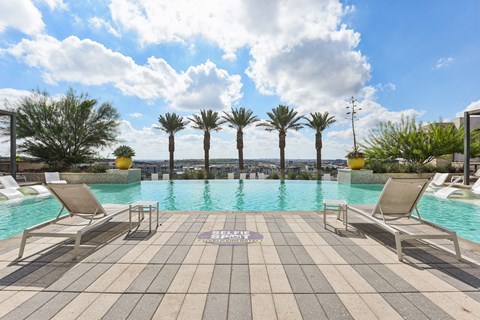 A pool surrounded by palm trees and lounge chairs.