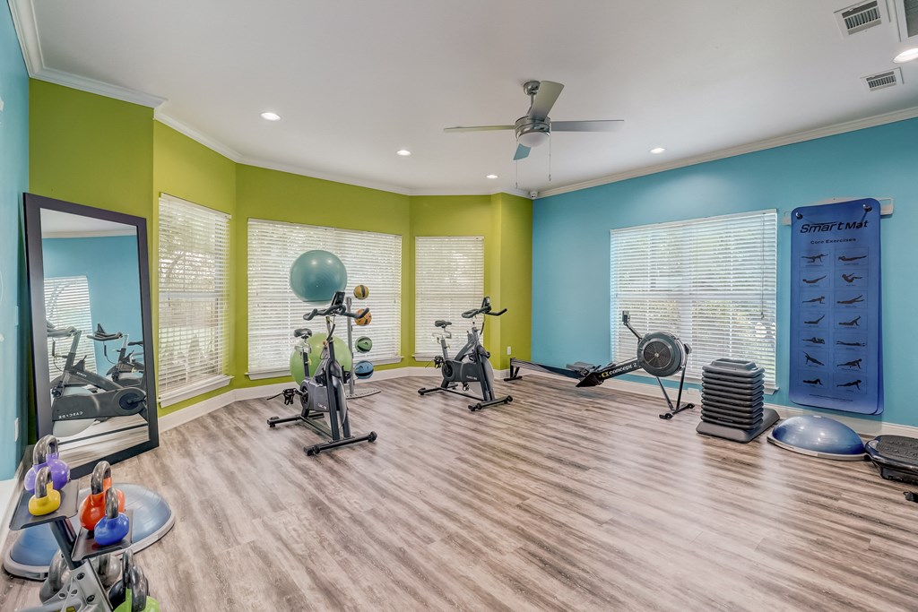 a workout room with weights and cardio machines and a ceiling fan
