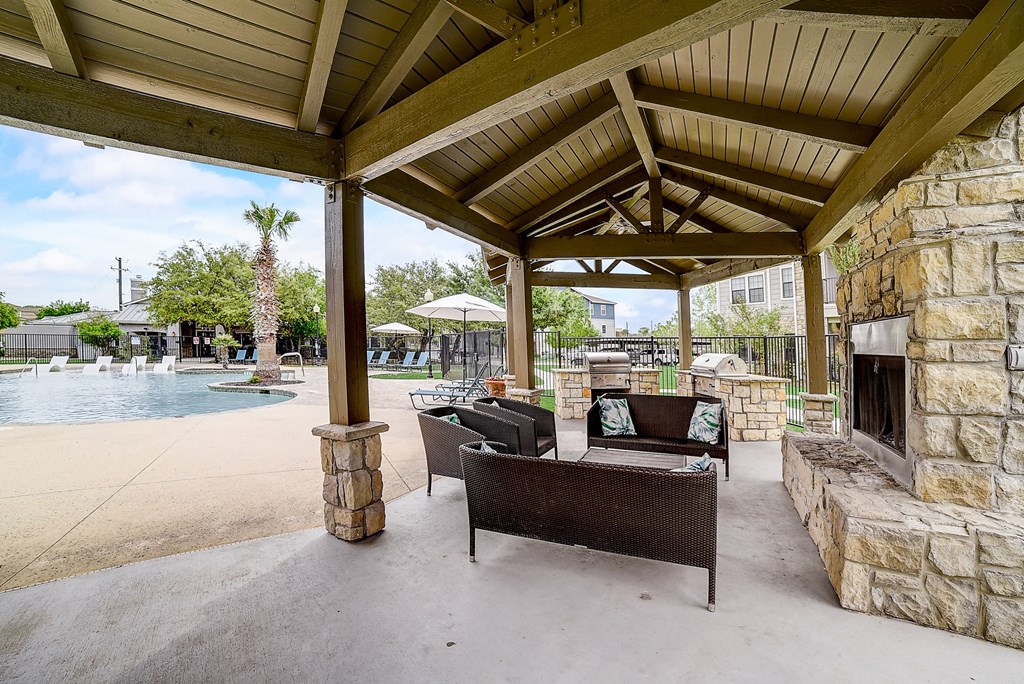 a covered patio with a fireplace and seating next to a pool