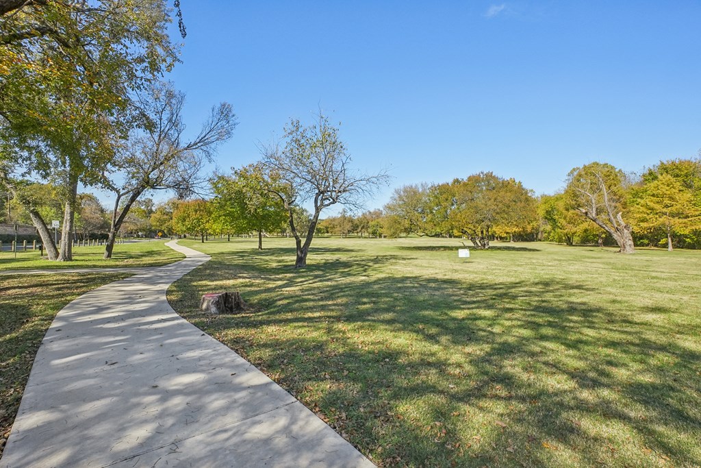 A concrete walkway leads through a grassy park with trees on either side.