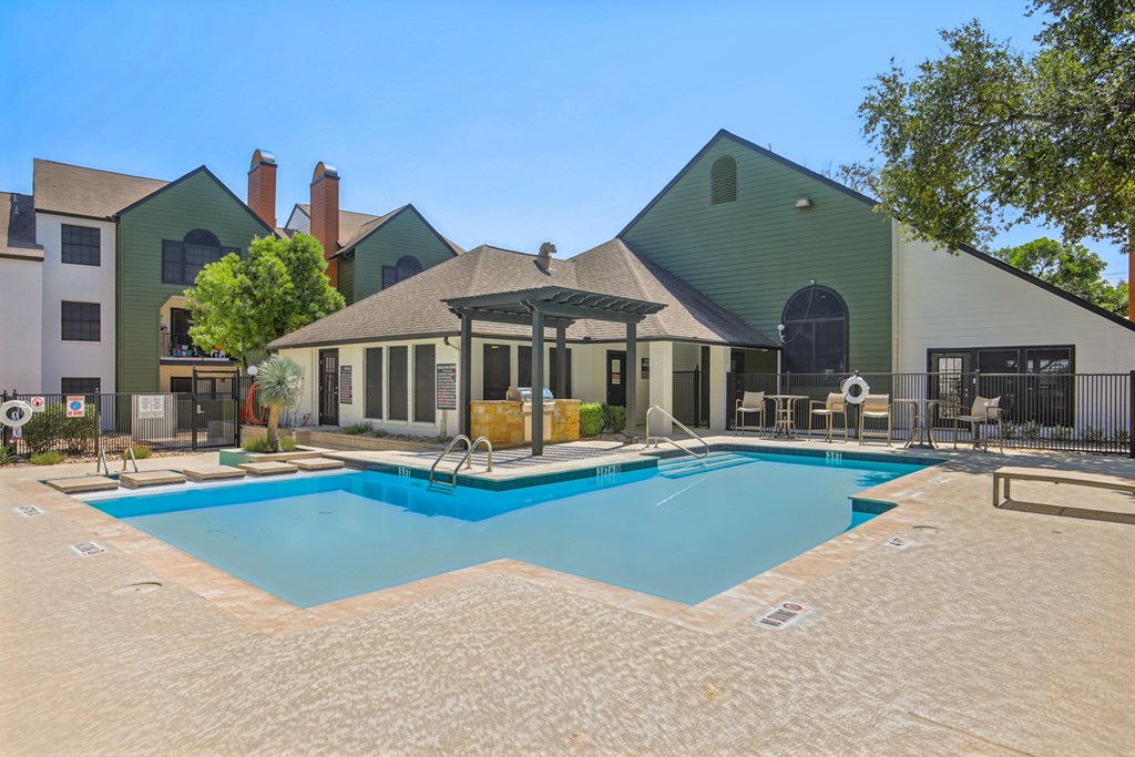 A large swimming pool in front of a house with a patio and a gazebo.