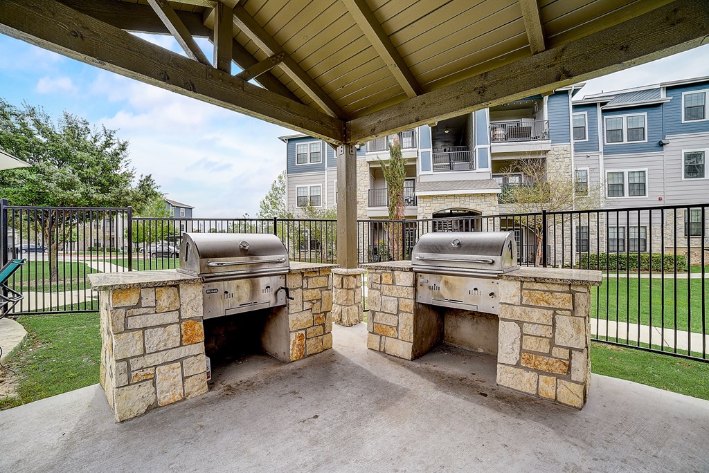 an outdoor kitchen with two bbq grills and a pergola