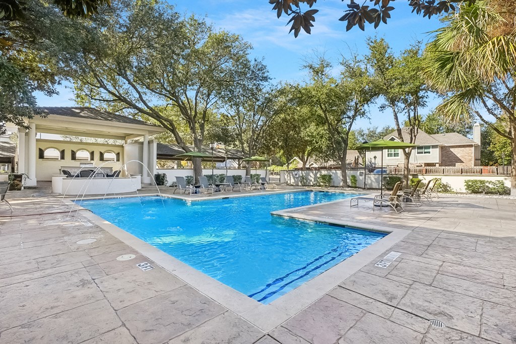 A large swimming pool surrounded by trees and a building in the background.