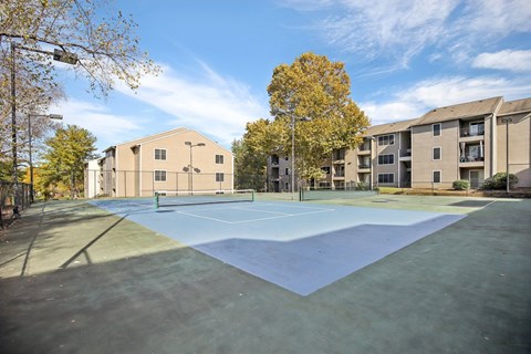A tennis court is surrounded by apartment buildings.