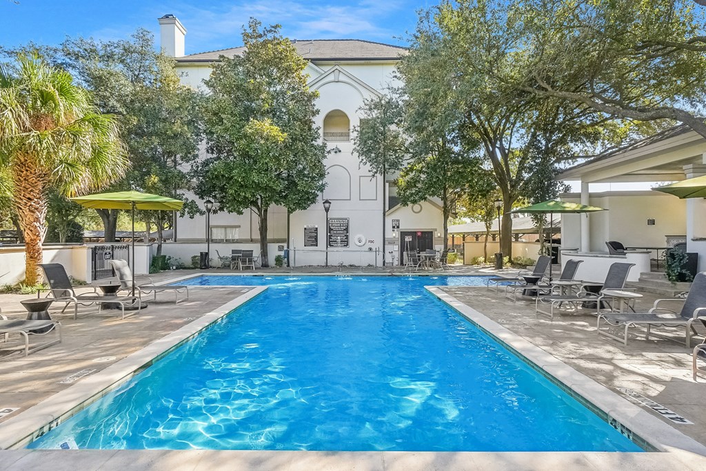 A large swimming pool surrounded by lounge chairs and trees.