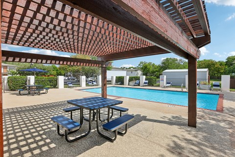 A picnic table with a blue top is in the foreground of a pool area.