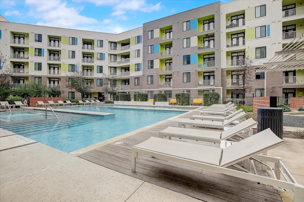 a swimming pool with white benches in front of an apartment building