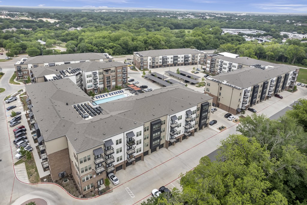 an aerial view of an apartment complex with a parking lot and trees