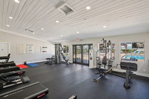 A spacious gym with a variety of equipment and a view of the pool outside.