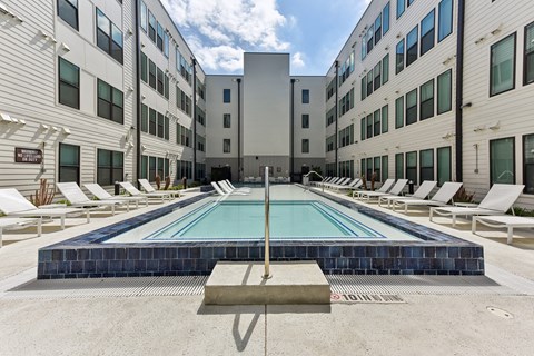 A large swimming pool surrounded by lounge chairs in front of a building.
