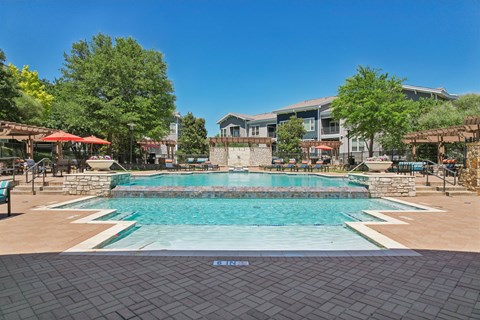 A large outdoor swimming pool surrounded by a stone wall and seating areas.
