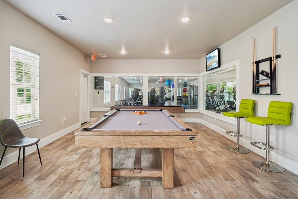 A pool table is in the middle of a room with a chair and a TV mounted on the wall.