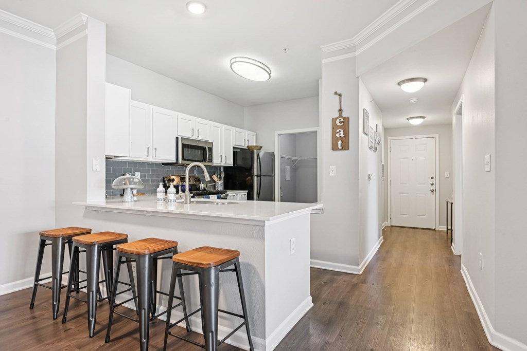 A kitchen with white cabinets and a white island with three stools.