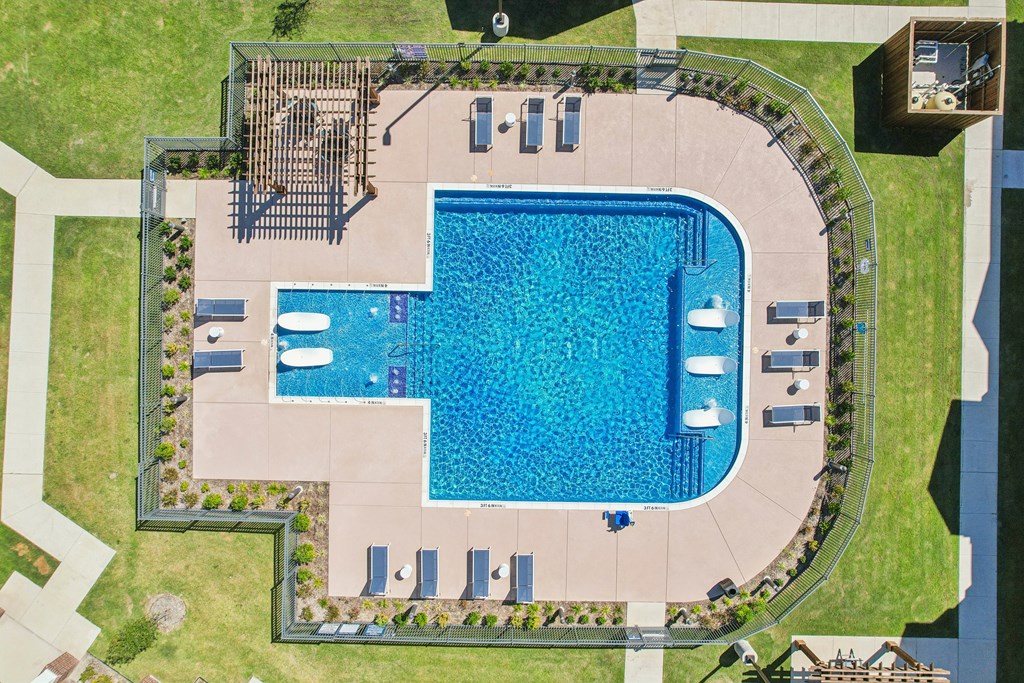 An aerial view of a swimming pool surrounded by a concrete patio and a grassy lawn.