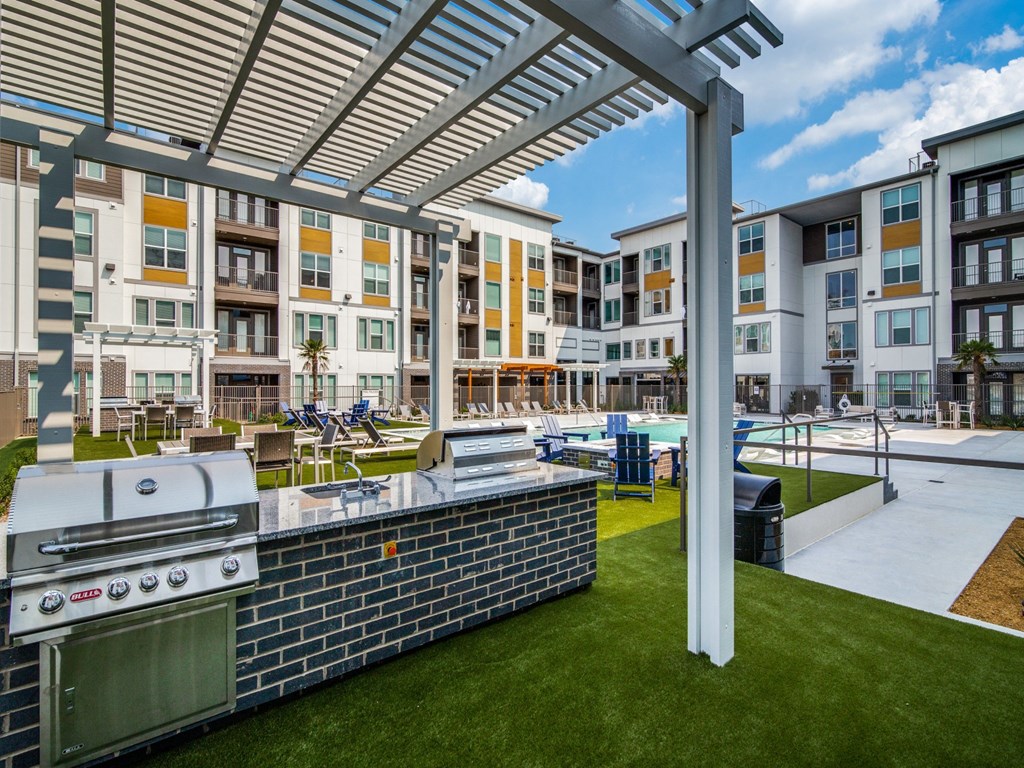 an outdoor kitchen with a grill and a pool in front of an apartment building
