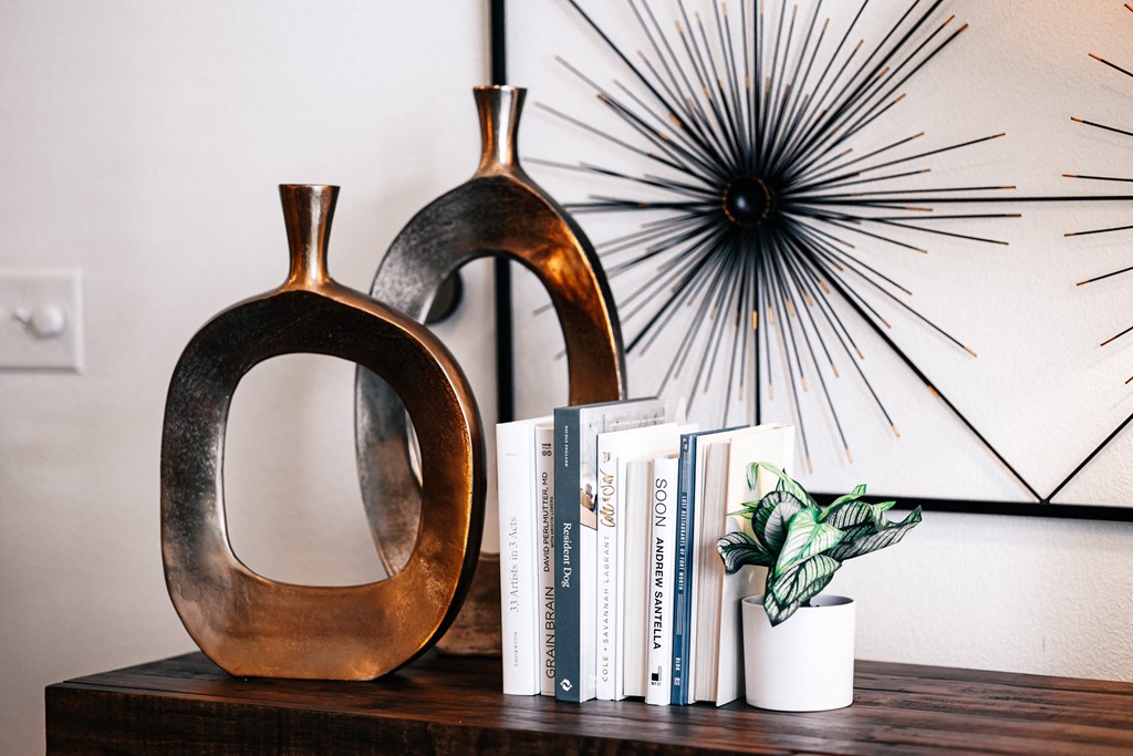 a shelf with two vases and books and a starburst mirror