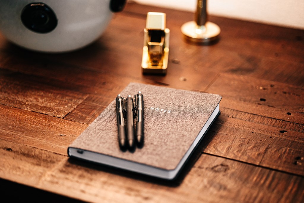 three pens sitting on top of a notebook on a wooden desk