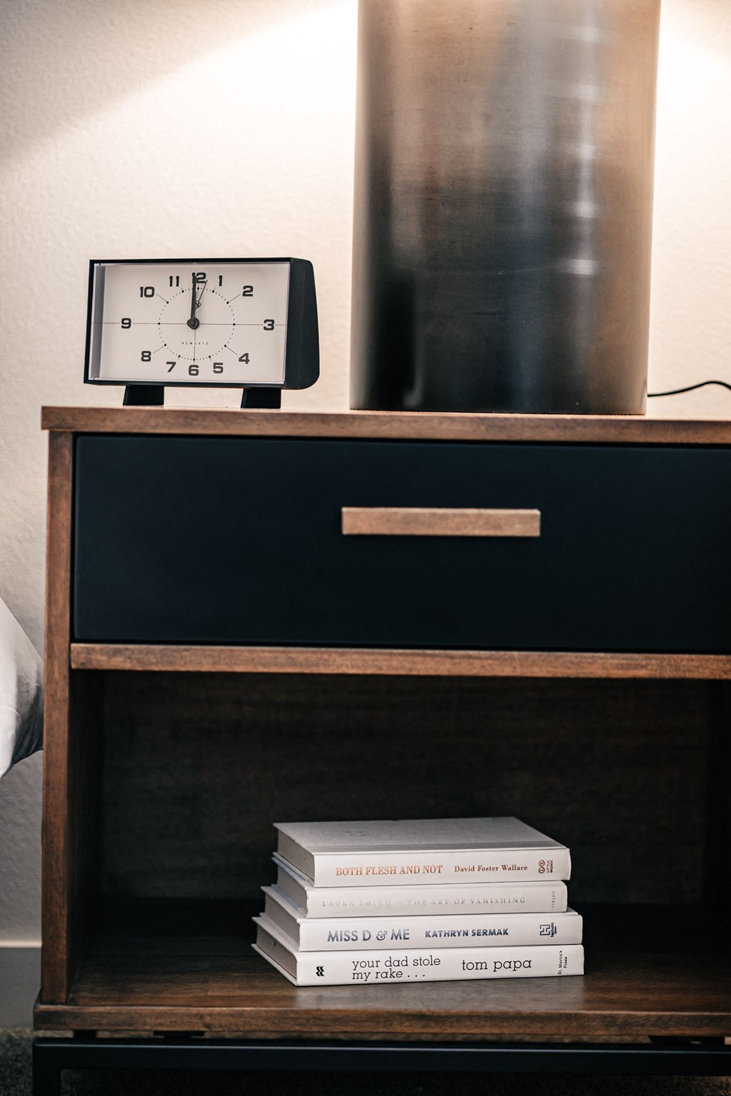 a stack of books on a nightstand with a clock and a drawer