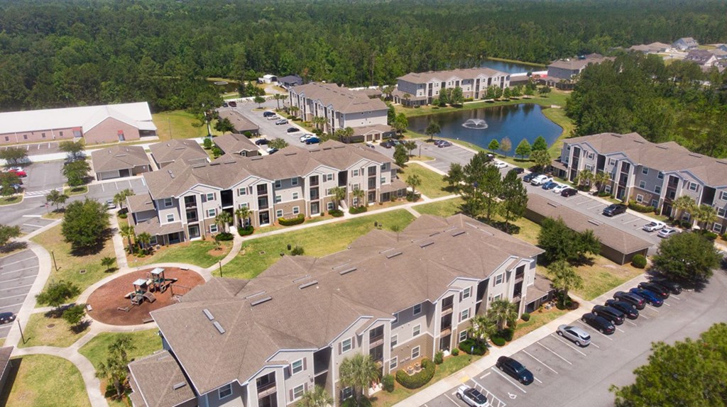 A bird's eye view of a residential complex with a pond and a playground.