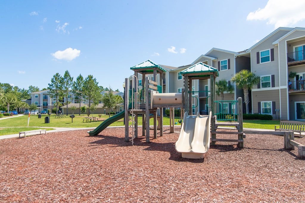 A playground with a green slide and a white slide in front of apartment buildings.