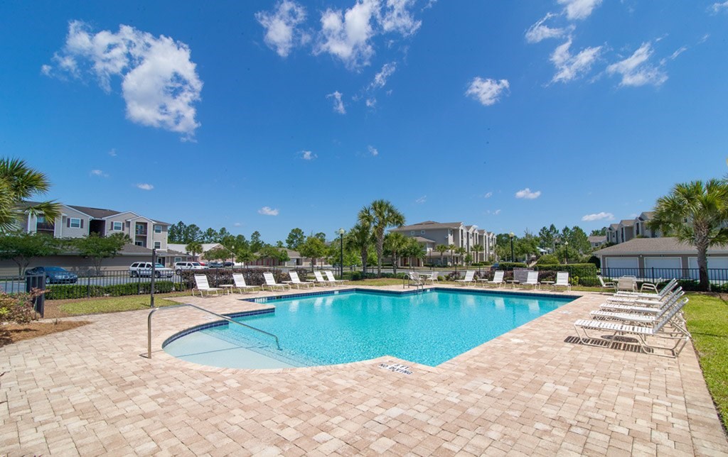 A large swimming pool surrounded by a brick patio and lounge chairs.