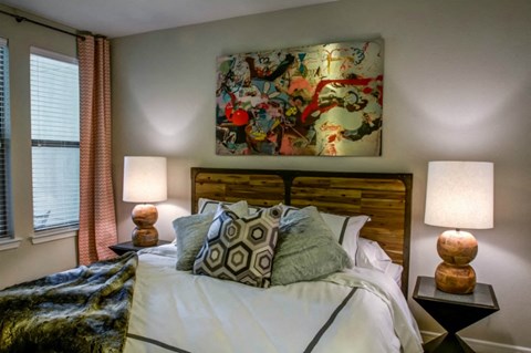 A bedroom with a large bed, two lamps, and a colorful painting on the wall.